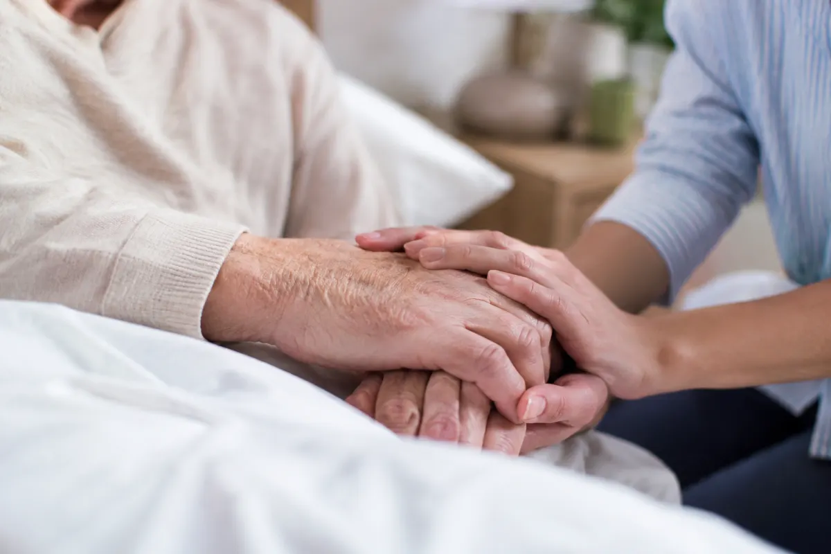 La loi fin de vie en France : ce qui a vraiment changé Mains d'un soignant tenant doucement la main d'un patient allongé dans un lit d'hôpital